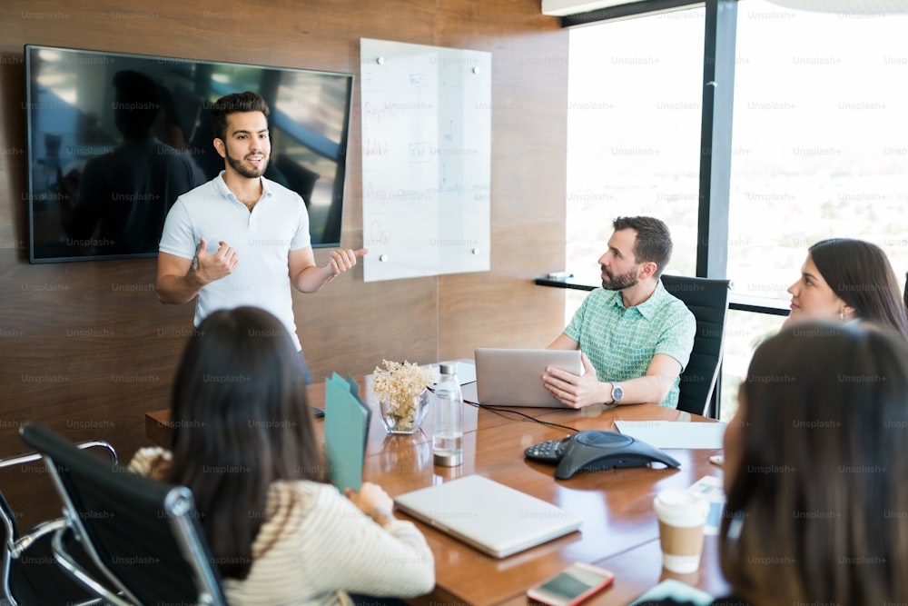 Young Hispanic presenter explaining business plan to coworkers in meeting room