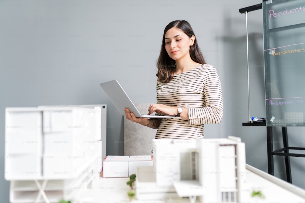 Confident businesswoman using laptop while analyzing model at architect office