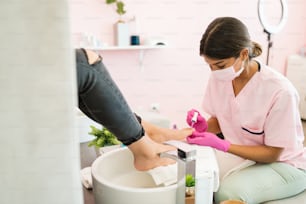 Joven esteticista arreglando las uñas de los pies del cliente durante la pedicura en el spa