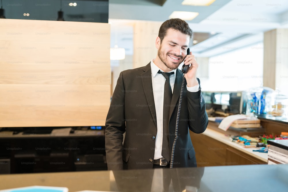 Manager maschio sorridente che conferma la prenotazione mentre parla di guardia alla reception nell'area della reception dell'hotel