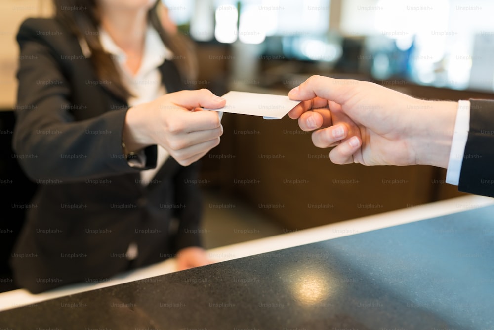Midsection of clerk giving card key to business professional at front desk in hotel