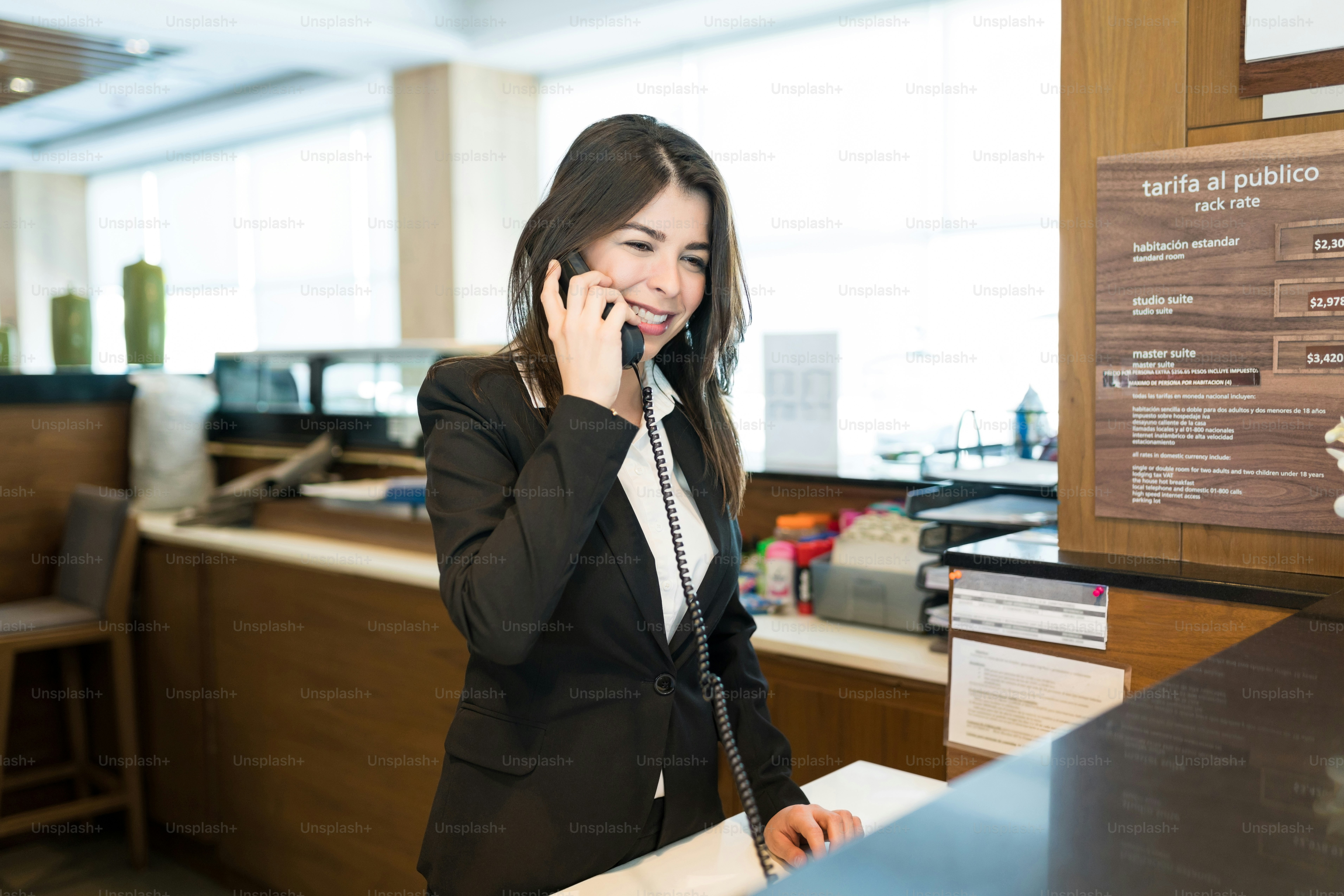 Pretty Latin professional talking on phone while standing at counter in reception area of hotel