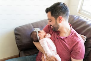 Latin dad carrying sleeping little girl while resting on sofa