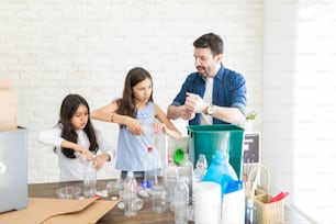 Padre adulto medio che insegna alle ragazze come schiacciare le bottiglie di plastica a casa
