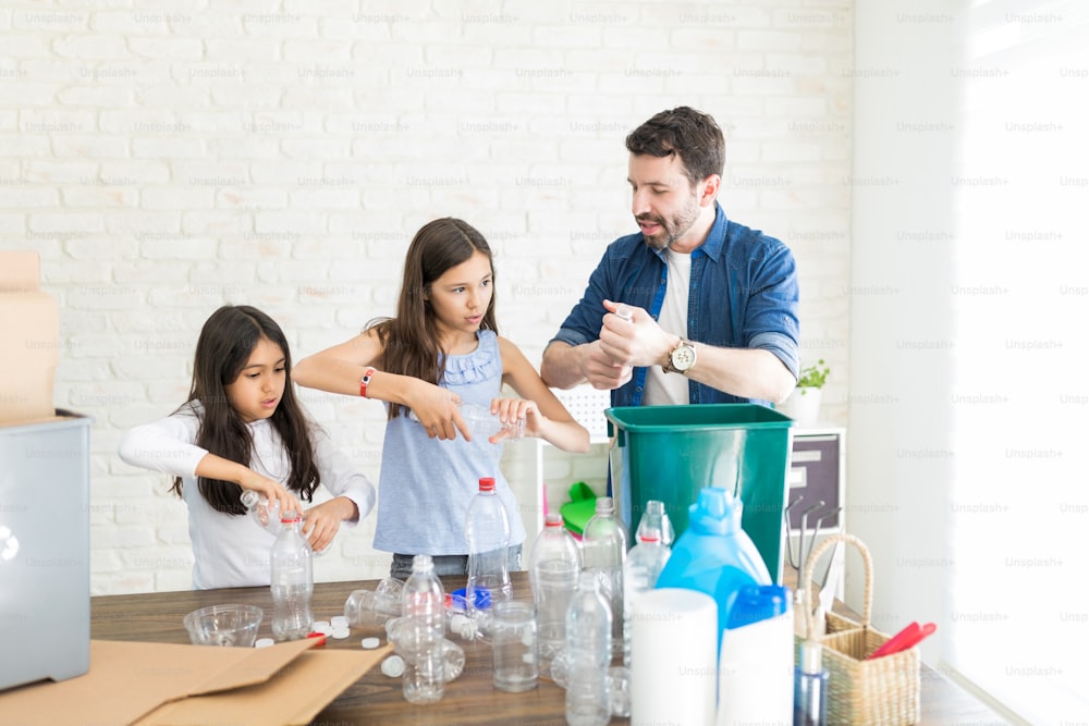 Padre adulto medio enseñando a las niñas a aplastar botellas de plástico en casa