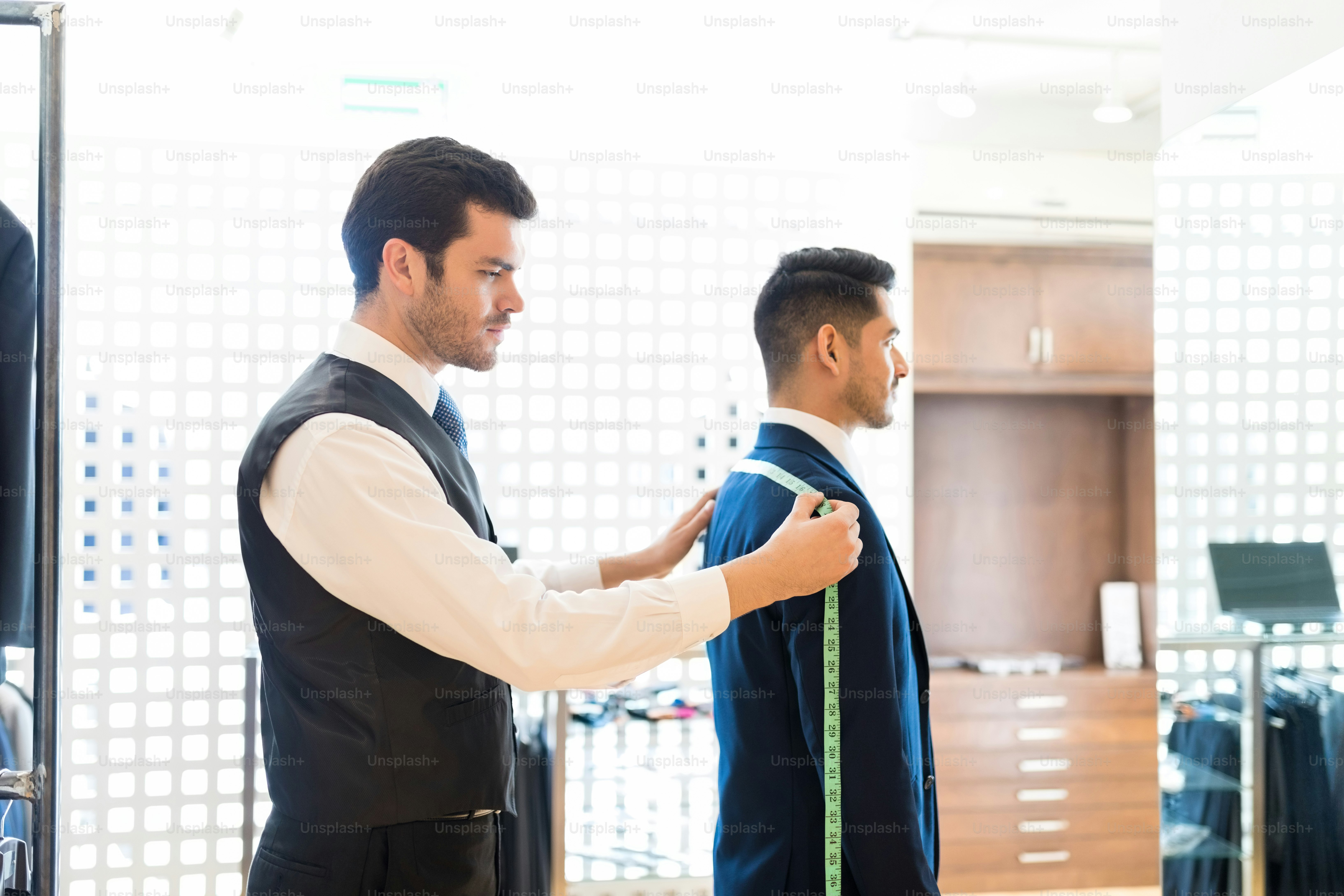 Seitenansicht des Tuchmachers, der die Rückenbreite seines Kunden mit Maßband im Laden misst