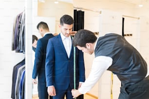 Young fashion designer taking measurement of man wearing elegant suit in tailor shop