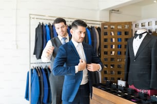 Empleado joven que ayuda al cliente a probarse el traje en la tienda de alquiler