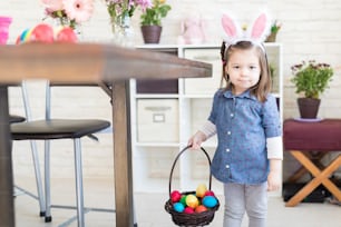 Portrait d’une douce fille portant un panier rempli d’œufs de Pâques à la maison