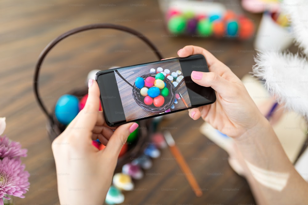 Closeup of hands photographing colorful Easter eggs on smartphone at home