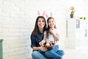 Portrait of cute daughter sitting on mother's lap while celebrating Easter at home