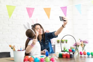 Mid adult woman taking self-portrait with loving girl kissing her and doing Easter artwork