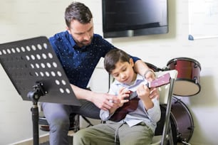 Hispanic male instructor giving ukulele lessons to boy in music school
