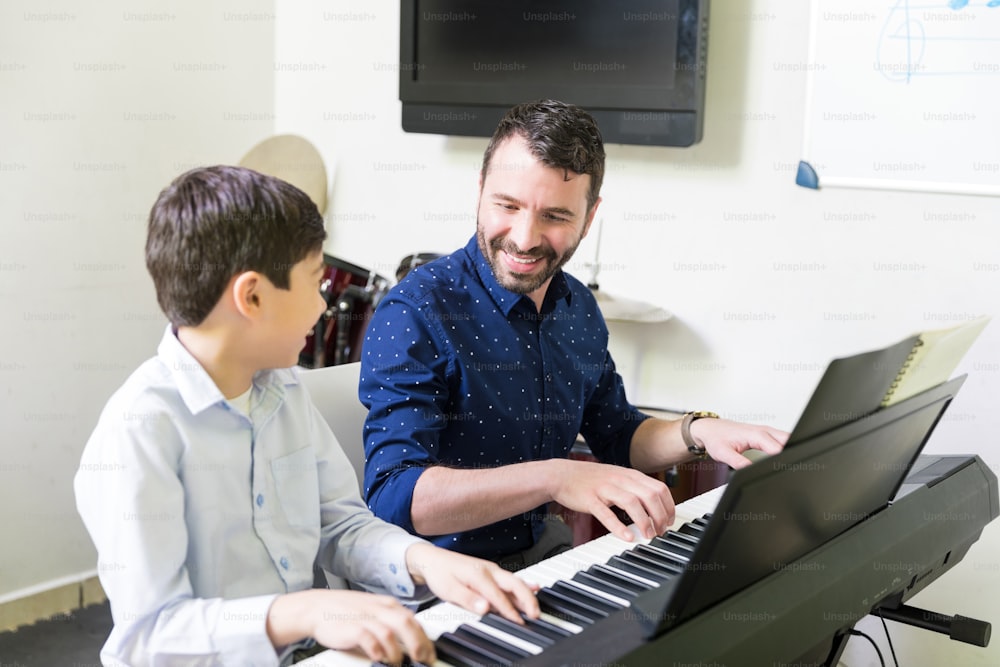 Smiling tutor training boy in playing sound synthesizer at music class