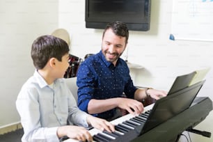 Smiling tutor training boy in playing sound synthesizer at music class