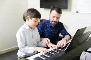 음악 아카데미에서 사운드 신디사이저 연주를 배우는 어린 학생을 돕는 남성 트레이너