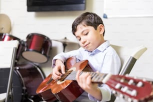 Niño seguro de sí mismo mejorando su velocidad de tocar la guitarra en la escuela de música