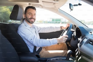 Selbstbewusster mittelerwachsener Besitzer, der auf dem Fahrersitz seines Autos sitzt und in die Kamera lächelt