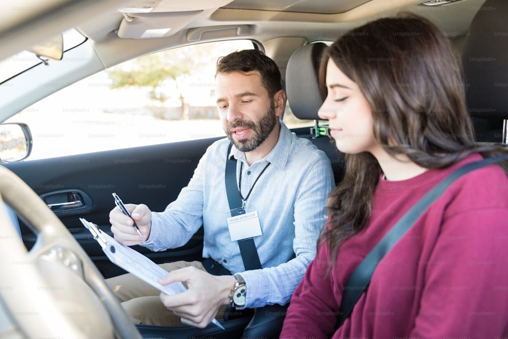 Mid adult Hispanic trainer showing checklist to student before car driving test