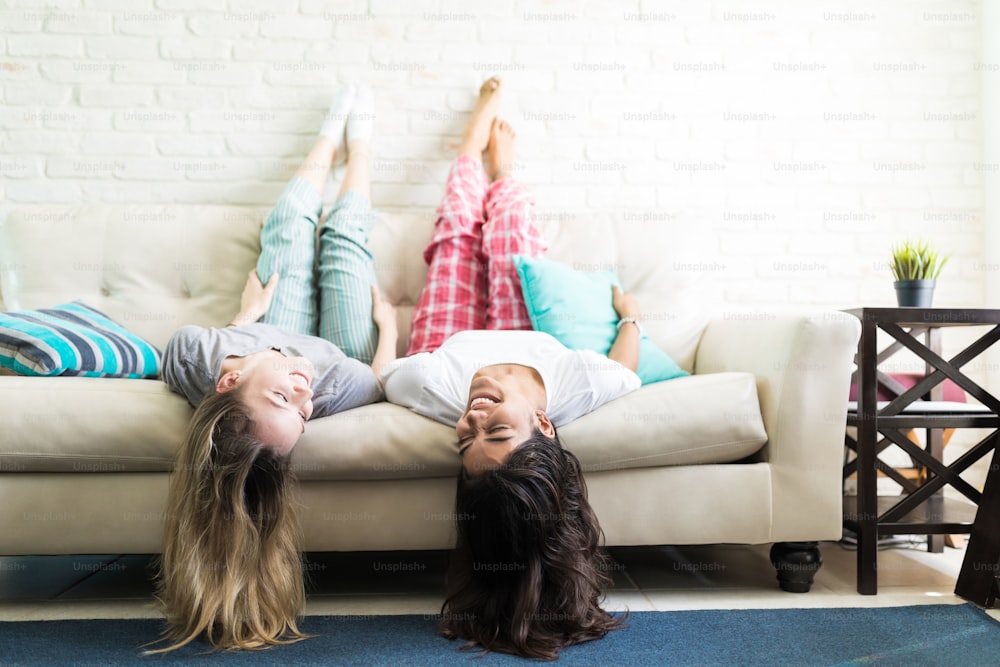 Happy female friends looking at each other while lying upside down on couch at home