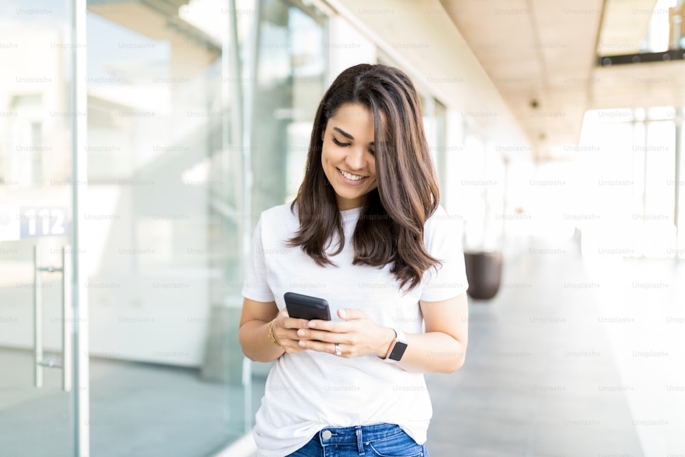 Femme adulte heureuse lisant la notification entrante sur le smartphone dans le centre commercial