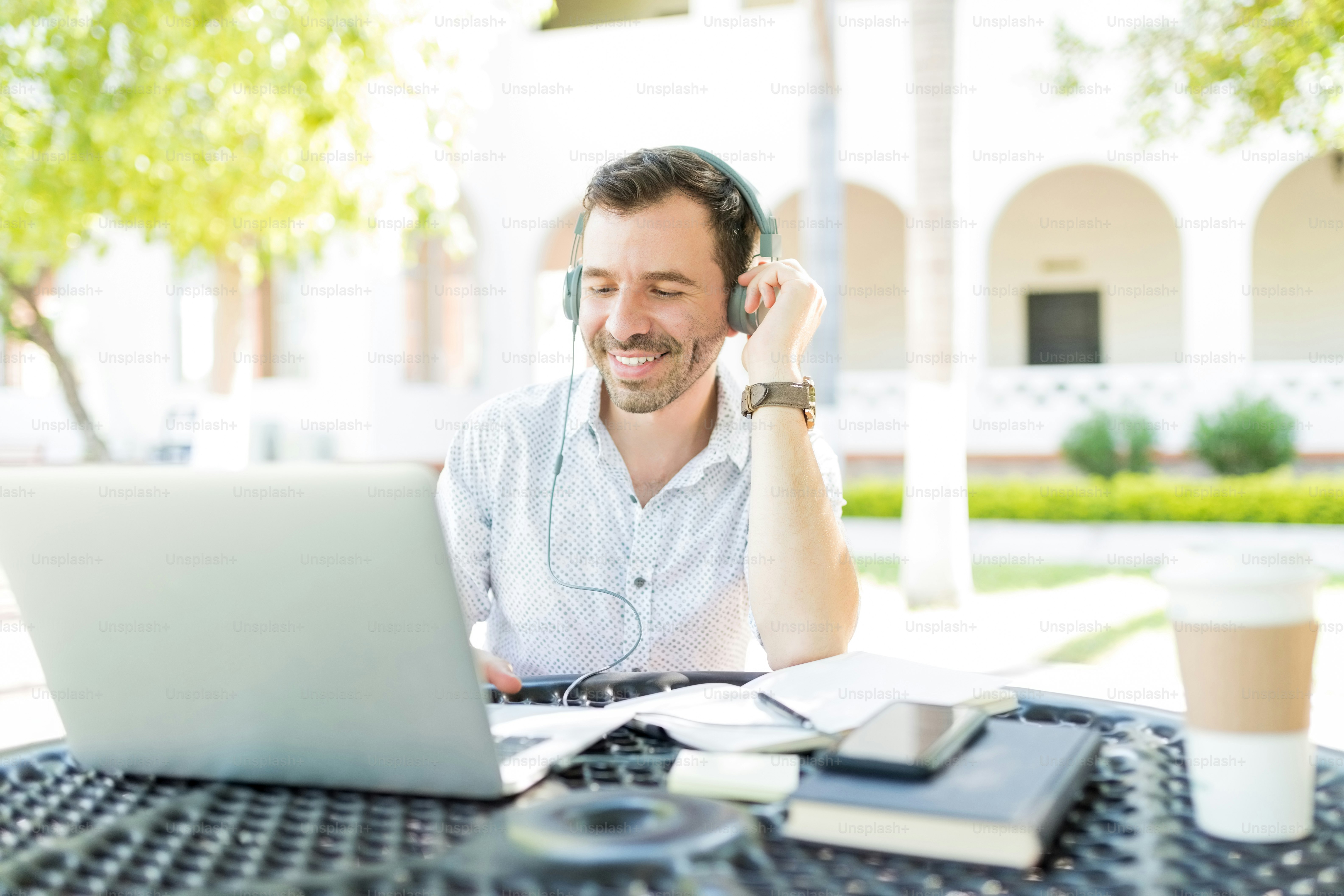 Smiling mid adult male using headphones connected to laptop while ...