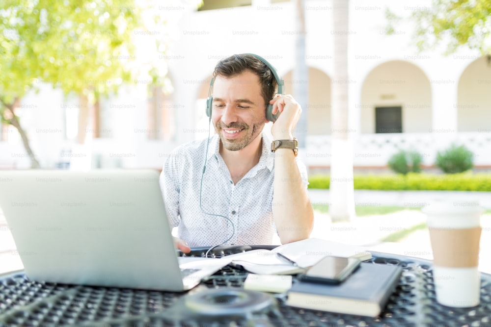 Smiling mid adult male using headphones connected to laptop while telecommuting in garden
