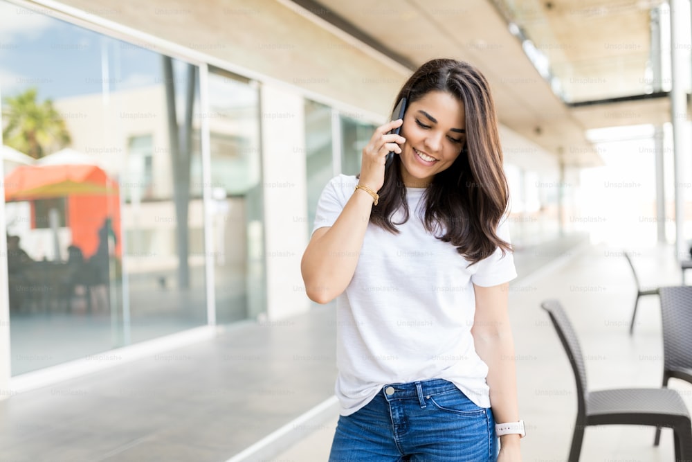 Mulher adulta média bonita falando no telefone móvel enquanto está em pé no shopping center
