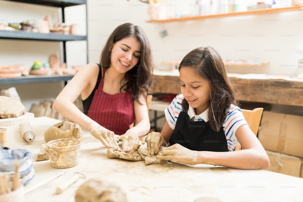 Woman and girl kneading clay to make art product at table in pottery workshop