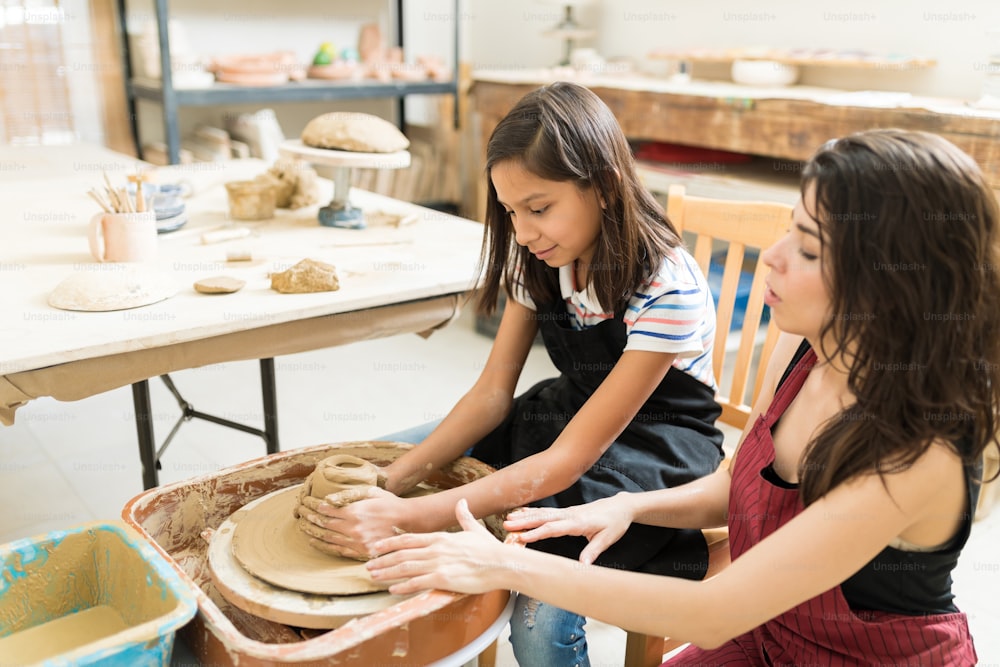 Female teacher teaching techniques of making pottery to girl in workshop