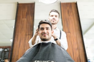 Confident man getting hair trimmed from young hairstylist in barber shop
