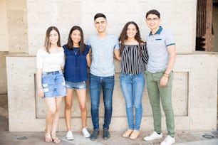 Portrait of group of five young friends standing together with arms around outdoors.