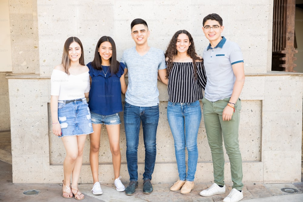 Portrait of group of five young friends standing together with arms around outdoors.