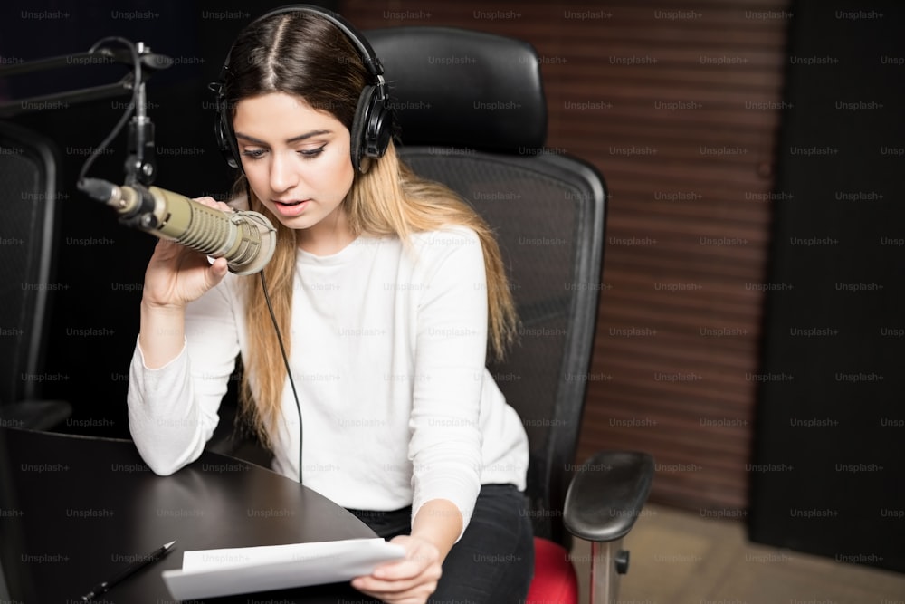 Frau, die als Radiosprecherin arbeitet, spricht mit einem Papier in der Hand über ein Mikrofon und sendet eine Live-Show auf Sendung