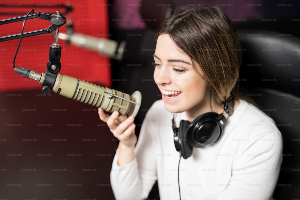 Selbstbewusste Radiomoderatorin, die in einem Radiosender in ein Mikrofon spricht und lächelt
