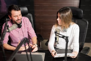Young male and female radio hosts talking with each other during a live radio show
