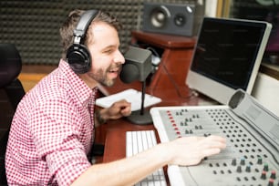 Hübscher junger Radiosprecher, der am Mikrofon spricht und die Sounds auf der gemischten Konsole anpasst