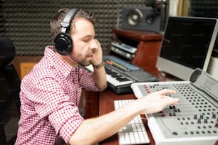 レコーディングスタジオでオーディオミキシングコンソールに取り組むヒスパニック系男性のサウンドエンジニア