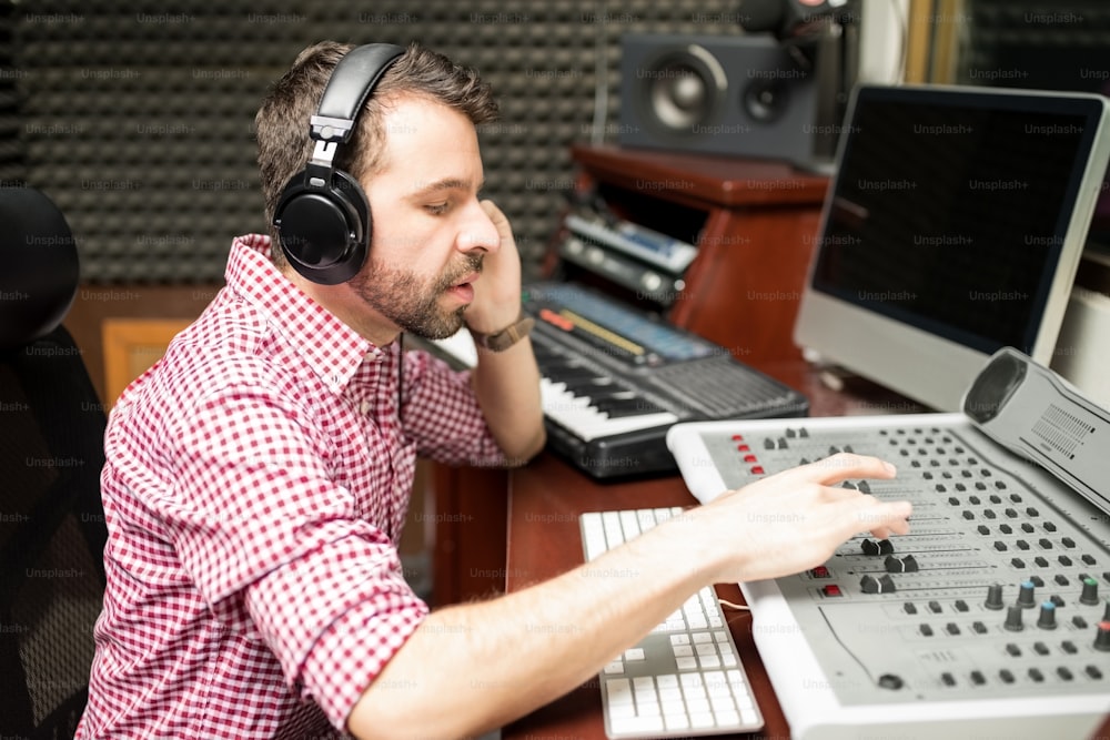 Engenheiro de som hispânico trabalhando em console de mixagem de áudio em estúdio de gravação