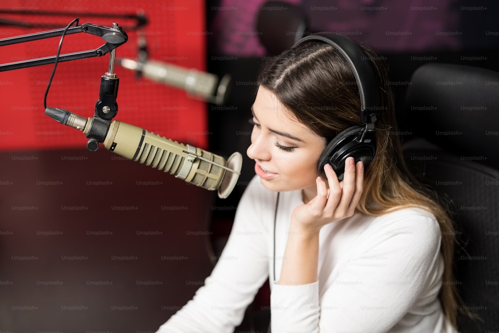 Nahaufnahme gut aussehende Radiosprecherin mit Kopfhörern, die über das Mikrofon im Studio senden
