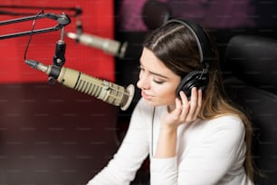 Close up good looking female radio announcer with headphones broadcasting through microphone in studio