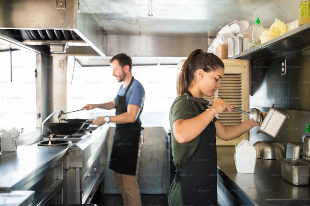 Two people cooking and serving some oriental food inside a food truck kitchen