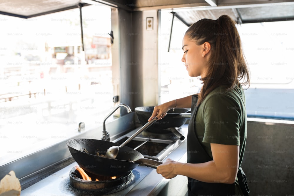Jolie jeune femme chef cuisinière cuisinant de la nourriture orientale dans un wok dans son food truck