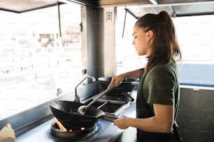 Bonita y joven chef cocinando algo de comida oriental en un wok en su camión de comida