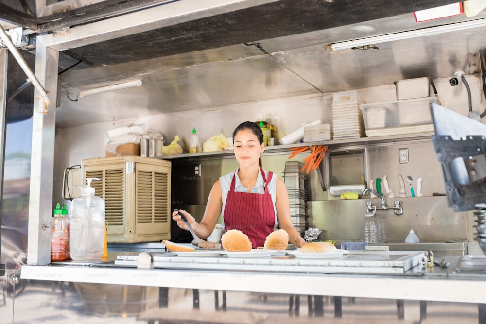 Ampia vista di una giovane cuoca che prepara alcuni hamburger mentre lavora in un camion di cibo