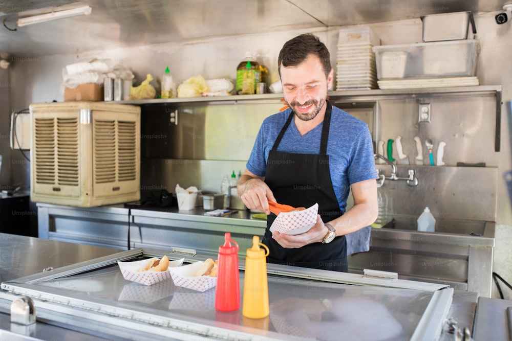 Attraktiver junger männlicher Koch, der in einem Food Truck kocht und Hot Dogs zubereitet