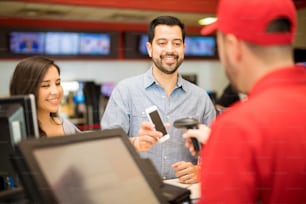 Un couple attrayant achète des billets au cinéma et utilise un smartphone pour montrer un code-barres à un employé