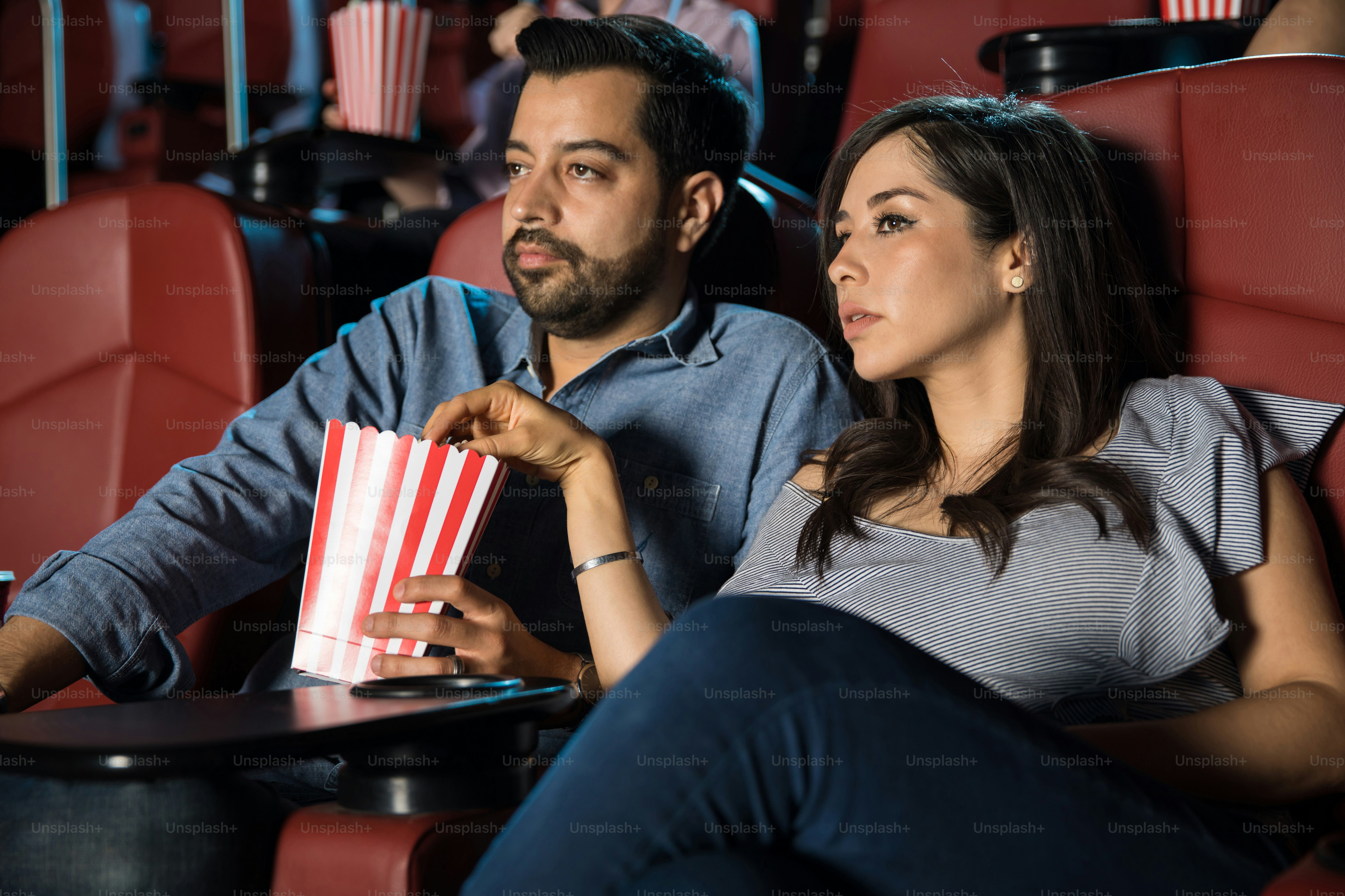 Good looking couple watching a thriller at the movie theater and eating ...