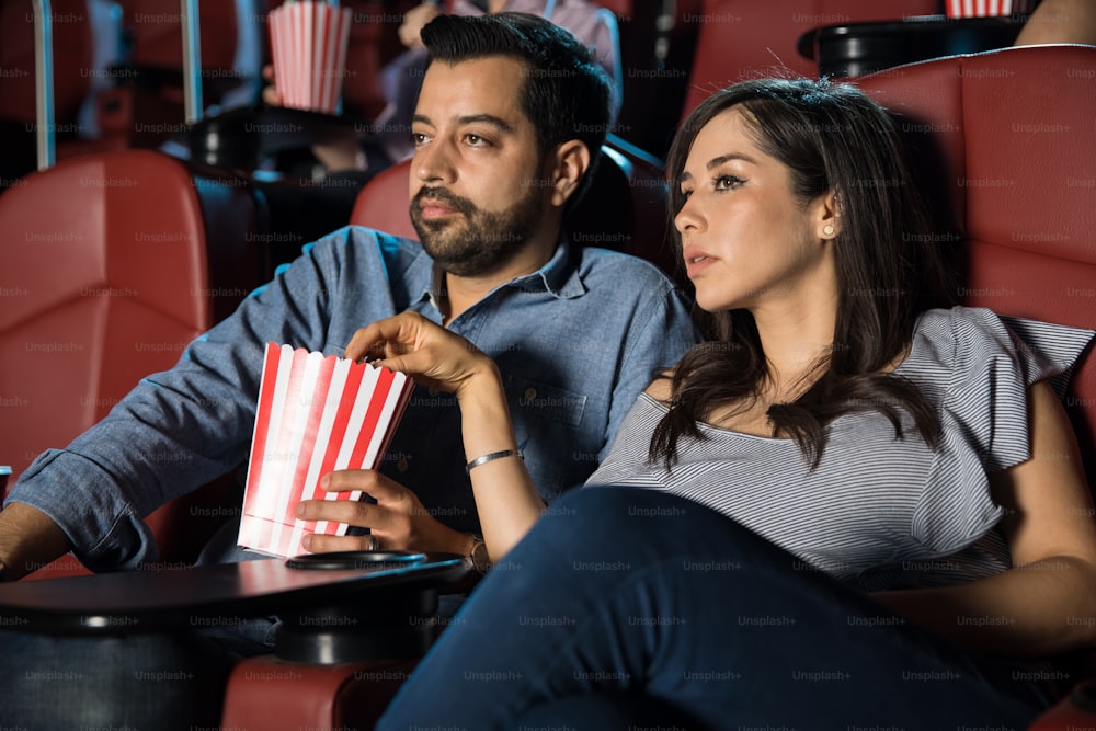 Good looking couple watching a thriller at the movie theater and eating some popcorn