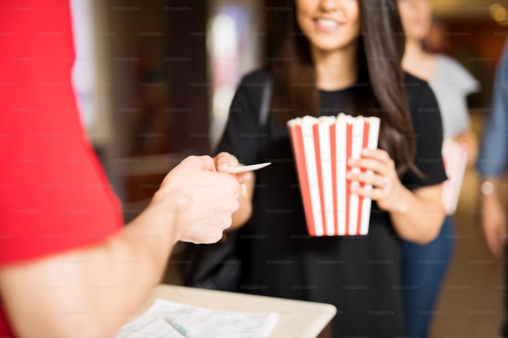 Primer plano de una mujer sosteniendo una bolsa de palomitas de maíz y entregando su boleto en la entrada del cine.